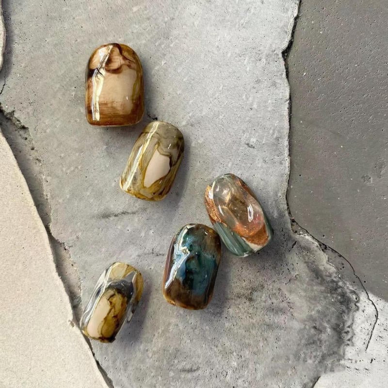 nail-van-da-dep__47__0cc11745e54e49bc8e7ece4c1ebfcab8 Bộ móng giả với họa tiết đá cẩm thạch, màu sắc đa dạng, nằm trên bề mặt xi măng xám.