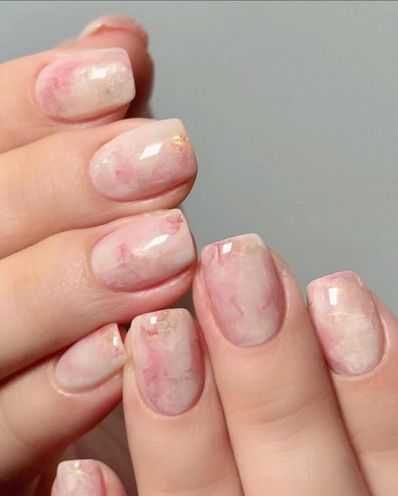 nail-van-da-dep__51__5aab91f45bf74f27ad22c817fcc281fc Bàn tay với móng tay được sơn màu hồng nhạt, có họa tiết đá cẩm thạch và ánh kim nhẹ.