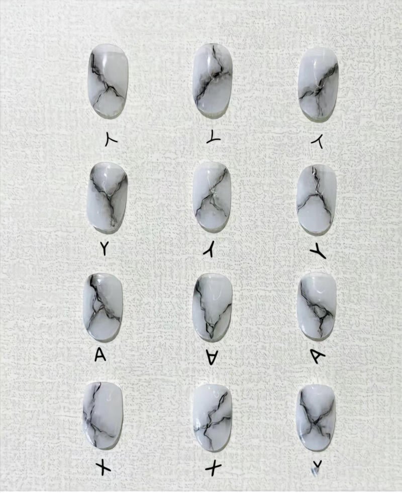 nail-van-da-dep__60__50a411d8df8c40909f389e7af7e797f9 Mẫu móng tay giả màu trắng với họa tiết vân đen, sắp xếp theo hai hàng dọc trên nền trắng.