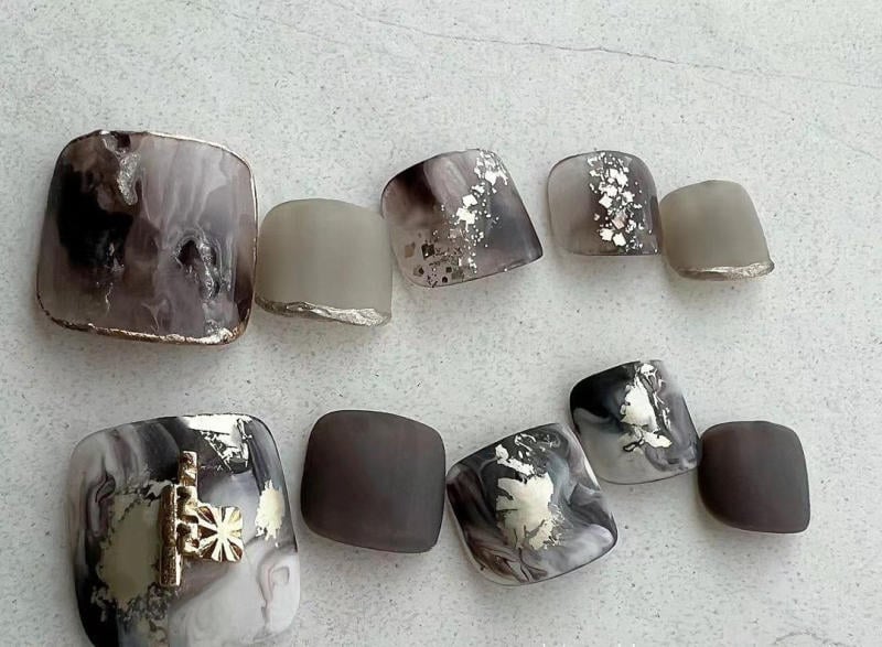 nail-van-da-dep__63__6c1462ebd7f344ba98e0ecf87cc57edd Bộ móng chân giả với thiết kế màu xám, trắng, kèm họa tiết hoa văn và ánh kim trên nền bề mặt nhám.
