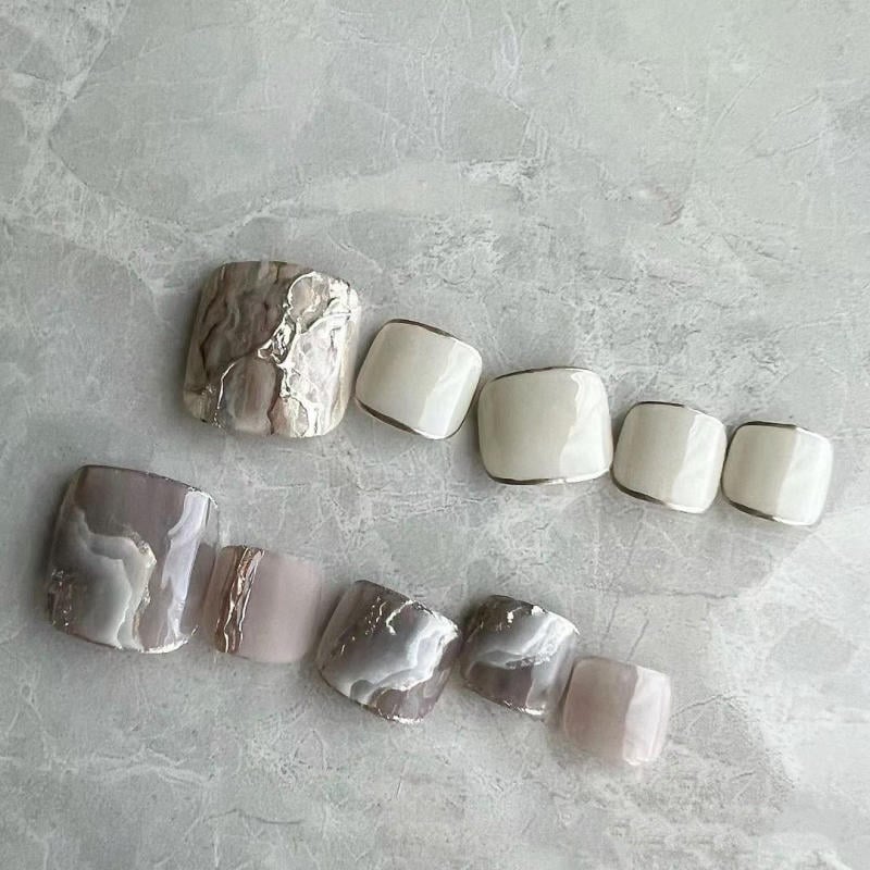 nail-van-da-dep__66__9fea5b39ca354d9db4468567b01c7047 Bộ móng giả với thiết kế màu sắc trung tính và họa tiết vân đá trên nền bề mặt màu xám nhạt.