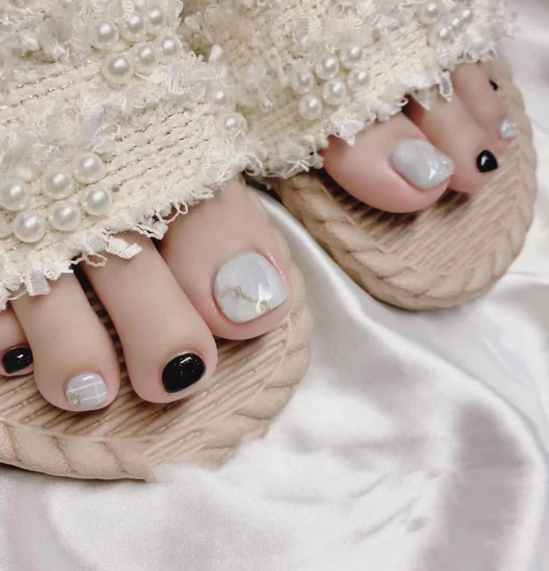 nail-van-da-dep__68__84eae2dbff7f40f0b61c87e822552555 Bàn chân với móng được sơn nghệ thuật, đi dép có trang trí ngọc trai, trên nền vải trắng.