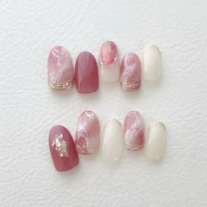 nail-van-da-dep__6__252af6f8019d4c6e8f08d174824a3126 Bộ móng giả màu hồng và trắng, với họa tiết nhũ bạc, được sắp xếp trên nền da trắng.