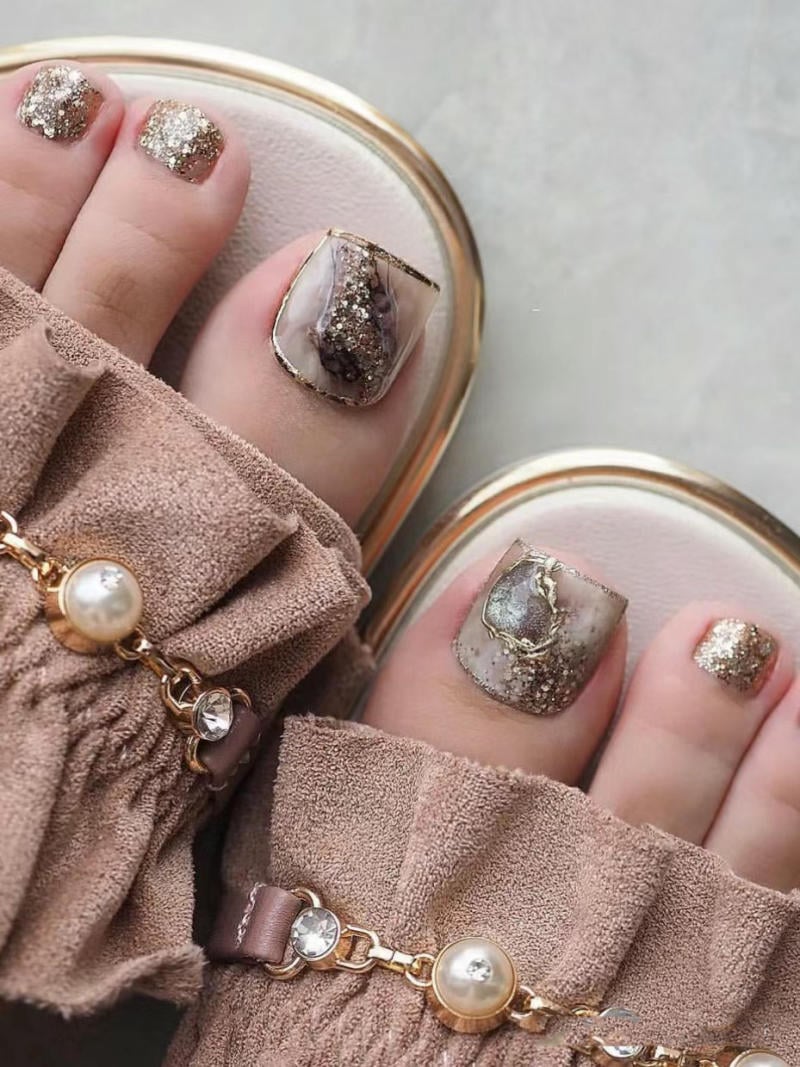 nail-van-da-dep__77__71f795e22c3240bbae40ebf06157fe19 Bàn chân với móng chân được sơn màu vàng nhũ và họa tiết đá cẩm thạch, đi đôi dép có trang trí ngọc trai.