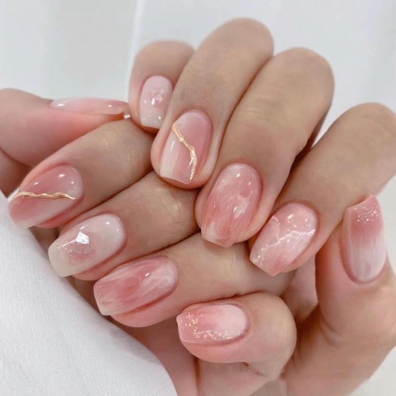 nail-van-da-dep__7__cfc9fa4d19cd43fab5668d4ee3c6e381 Bàn tay với móng tay được sơn màu hồng nhạt, có họa tiết trang trí tinh tế và sáng bóng.