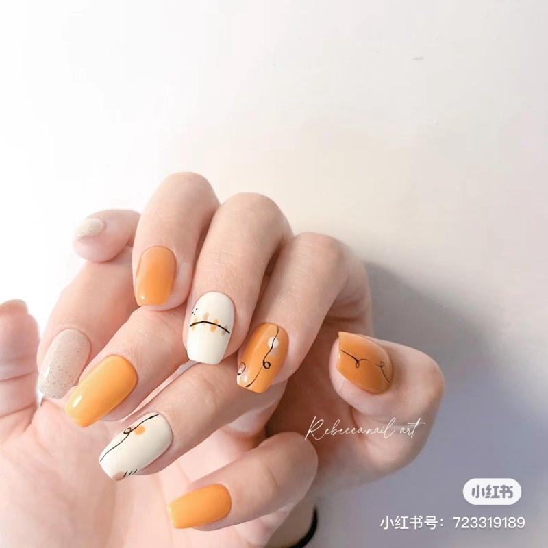 Bàn tay với móng nghệ thuật màu cam và trắng, họa tiết đơn giản trên nền trắng và cam.