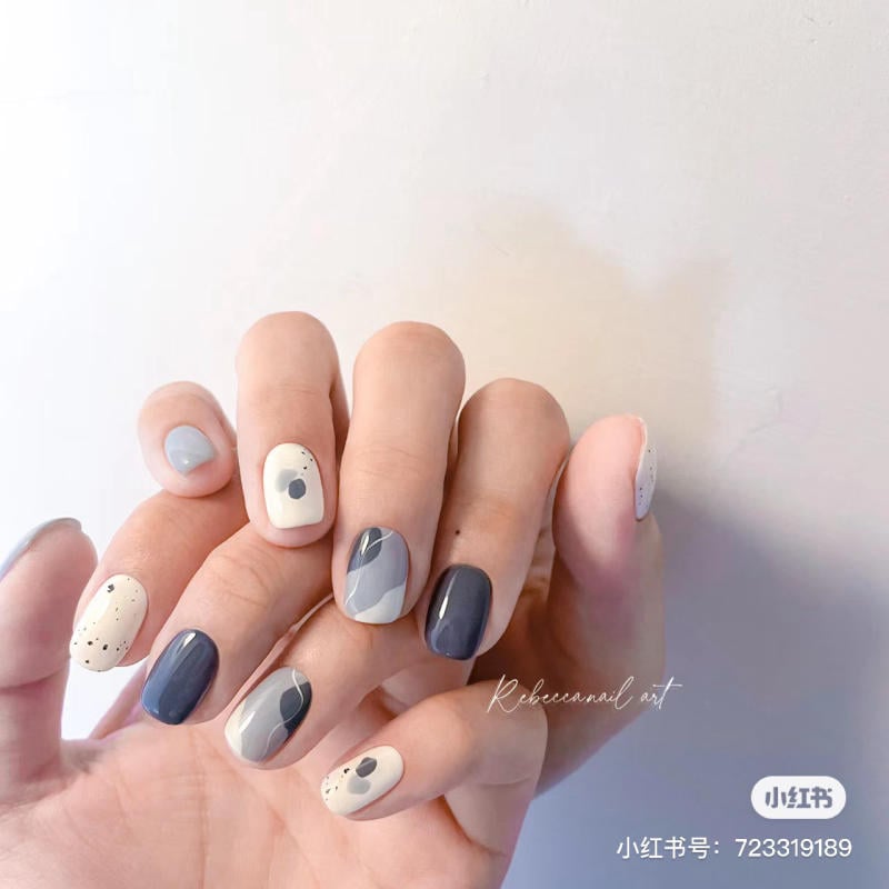 Tay với móng tay được sơn nghệ thuật, phối màu xám và trắng, có họa tiết chấm và hình học.