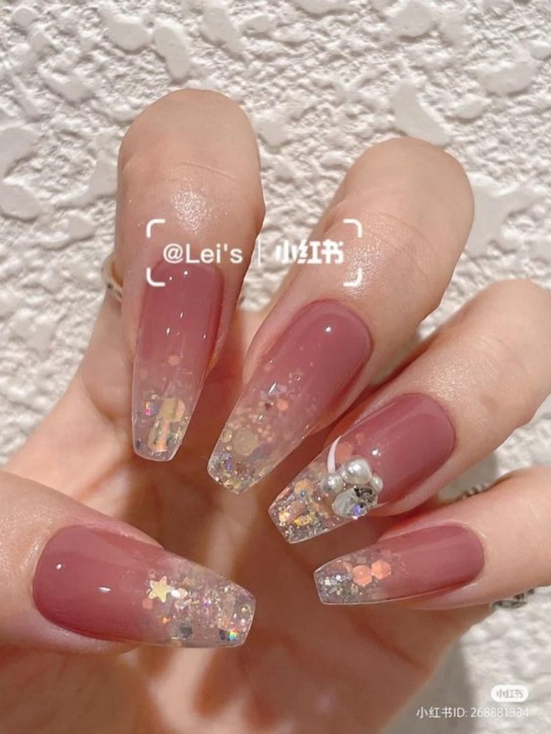 Bàn tay với móng tay được sơn màu đỏ nhạt, trang trí lấp lánh và đính đá.