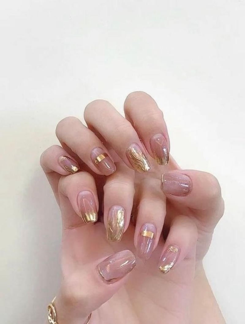 Bàn tay với móng tay được sơn màu hồng nhạt và trang trí họa tiết vàng kim loại.