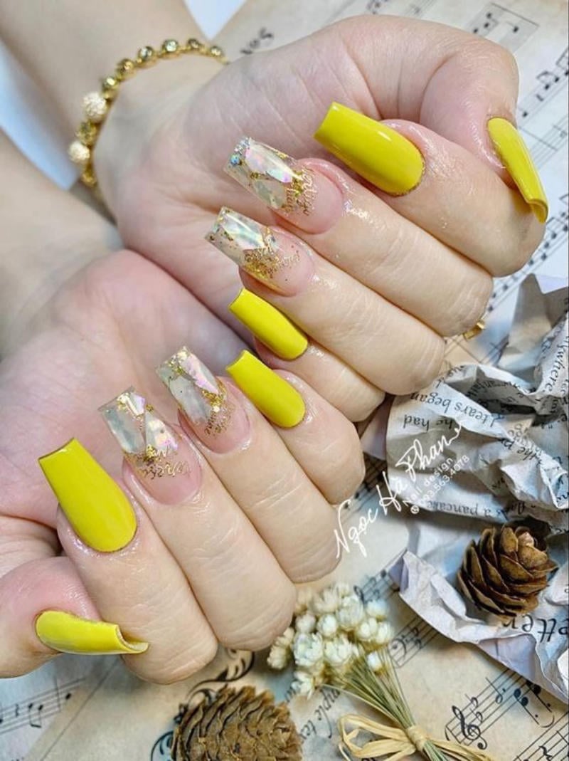Bàn tay với móng tay được sơn màu vàng và trang trí lấp lánh. Nền có nốt nhạc và đồ trang trí nhỏ.