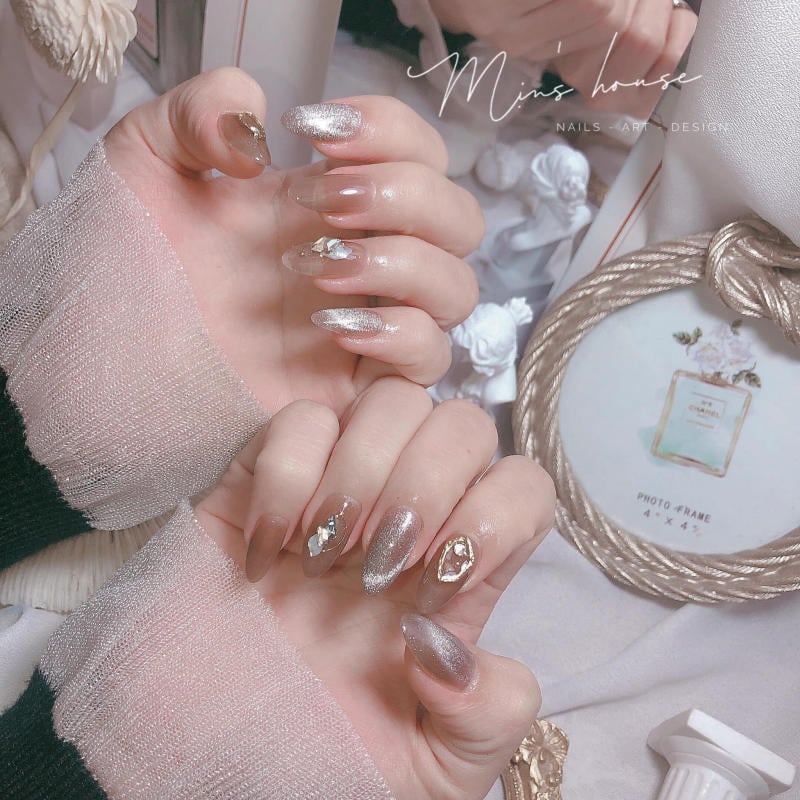 Bàn tay với móng tay được trang trí lấp lánh, đặt trên nền có các phụ kiện nghệ thuật và khung ảnh.