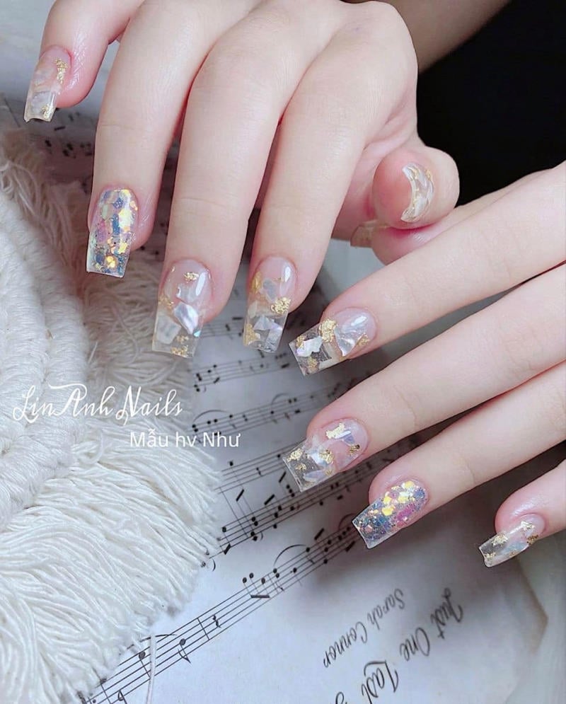 Bàn tay với móng tay được trang trí họa tiết lấp lánh, đặt trên nền giấy nhạc và vải mềm.