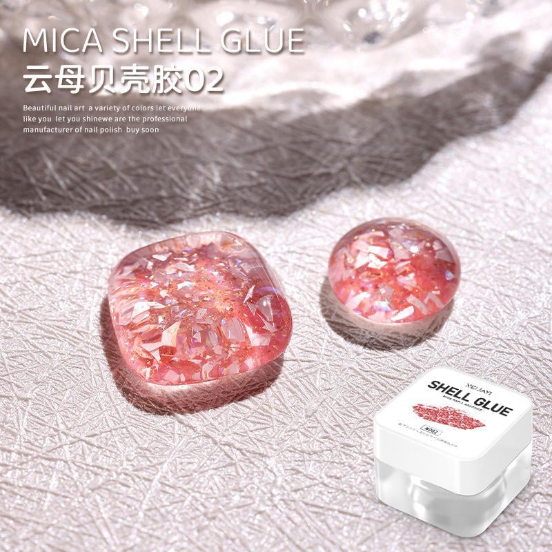 Hộp keo vỏ sò mica màu hồng ánh, đặt cạnh hai mẫu móng tay giả trên nền sáng.