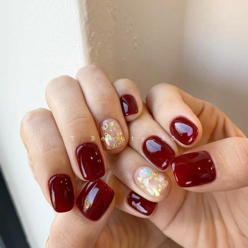 Bàn tay với móng tay được sơn màu đỏ đậm, một móng có họa tiết trang trí ánh vàng.