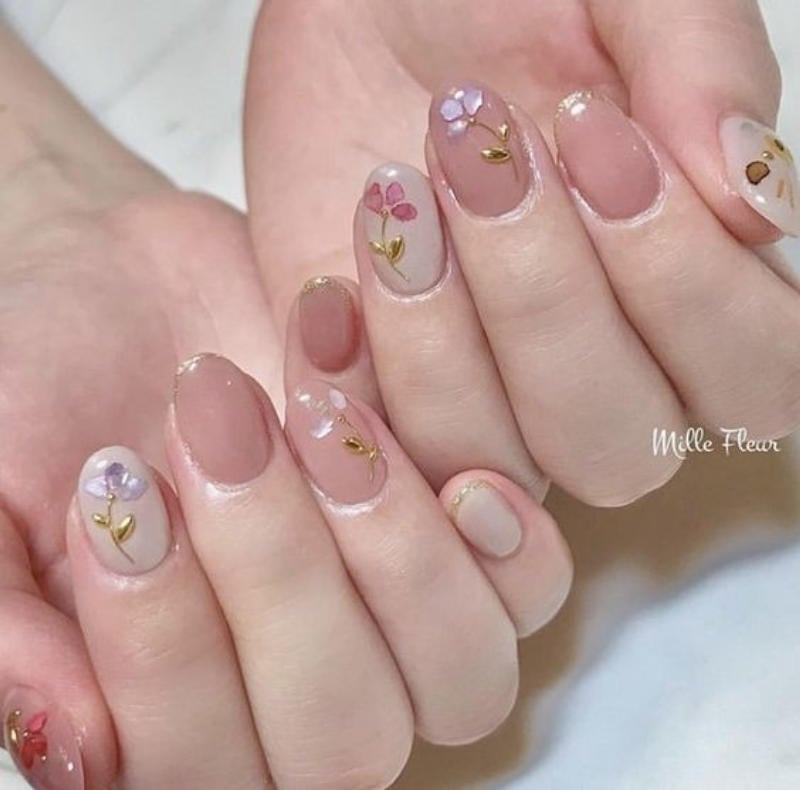 Bàn tay với móng tay được trang trí hoa nhỏ, tông màu nude và hồng nhạt, tạo kiểu tinh tế và nhẹ nhàng.