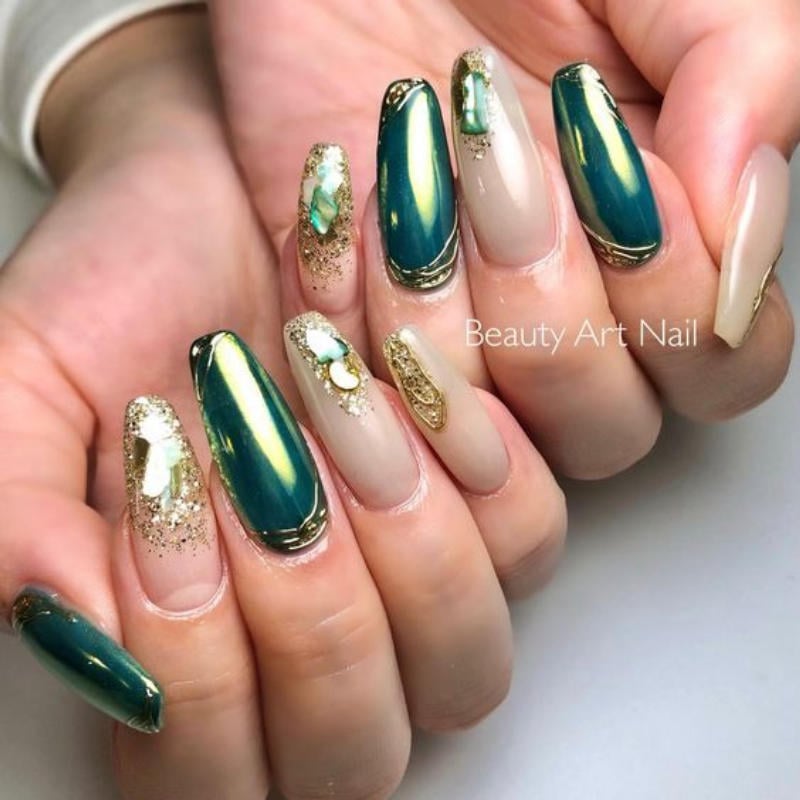 Bàn tay với móng tay dài được trang trí họa tiết xanh lá, vàng và kim tuyến.