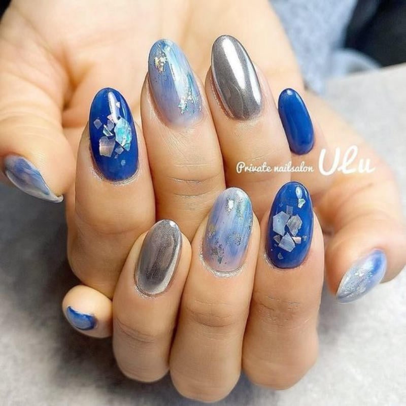 Bàn tay với móng tay được sơn màu xanh, bạc và đính đá lấp lánh.
