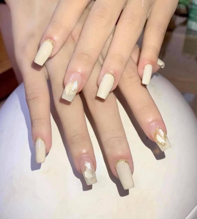 Bàn tay với móng tay dài được sơn màu trắng kem và trang trí họa tiết vàng.