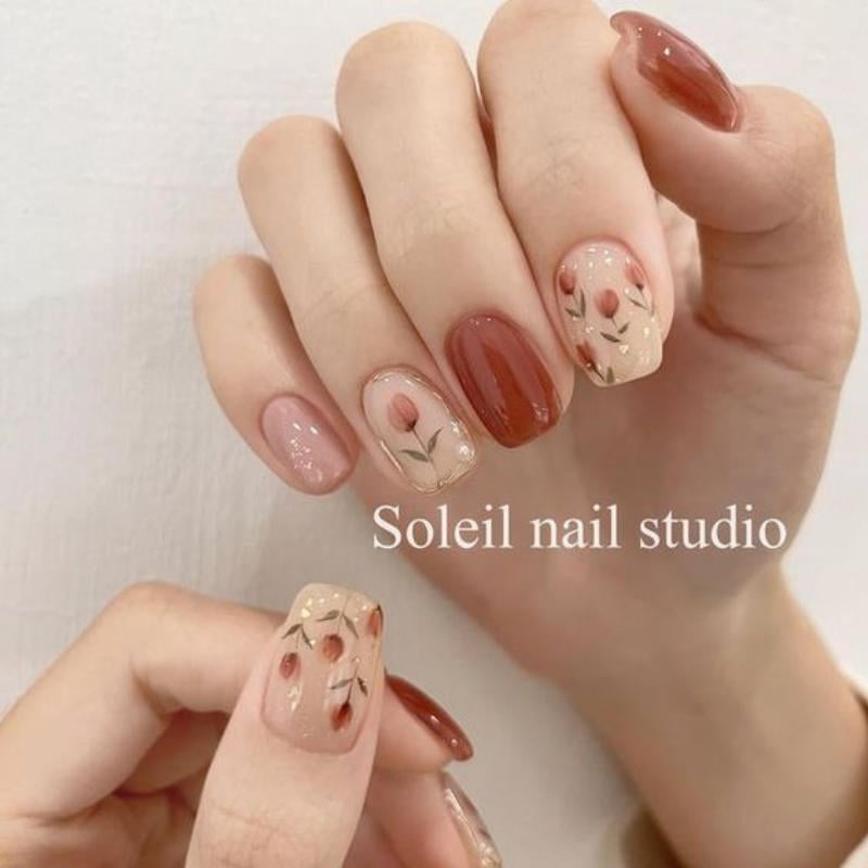 Bàn tay với móng tay được sơn màu nâu và trang trí họa tiết hoa tinh tế, nền trắng.