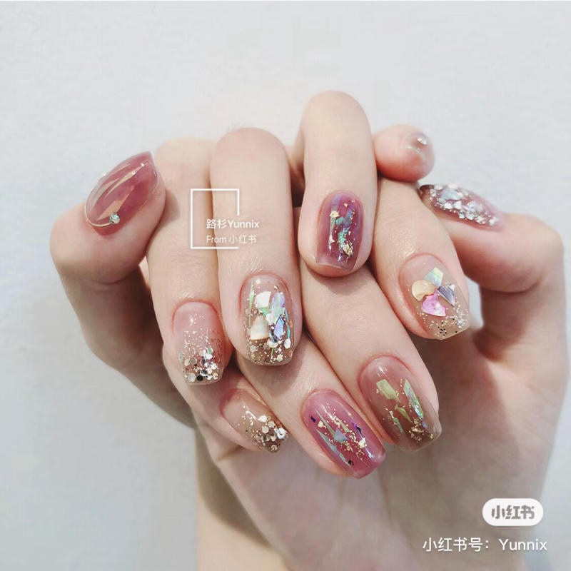 Bàn tay với móng tay được sơn màu hồng nhạt và đính đá lấp lánh nhiều màu sắc.