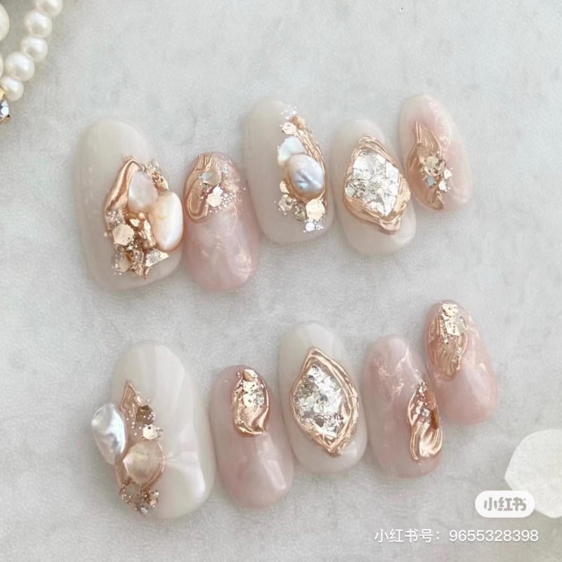 Bộ móng tay giả với thiết kế họa tiết nổi và màu sắc nhẹ nhàng trên bề mặt trắng, ánh vàng và hồng nhạt.