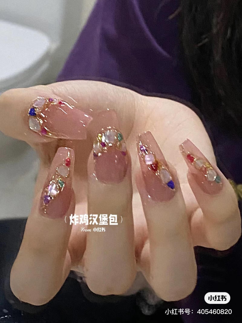 Bàn tay với móng tay dài, được trang trí bằng đá quý nhiều màu sắc và họa tiết lấp lánh.