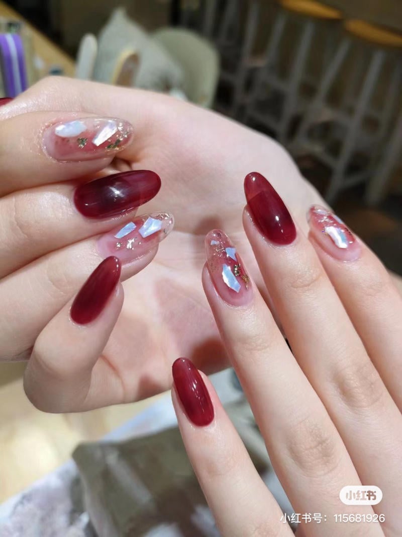 Bàn tay với móng tay sơn màu đỏ và trang trí họa tiết lấp lánh, nền mờ với ghế và bàn.