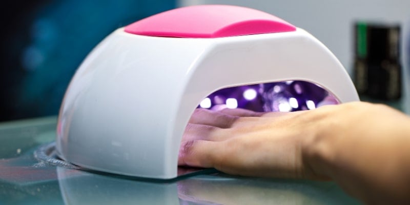 Bàn tay đang được đặt dưới đèn UV màu trắng và hồng dùng để làm khô móng trên bàn.