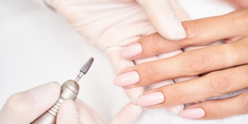 Người đang sử dụng dụng cụ để chăm sóc móng tay với lớp sơn màu hồng nhạt trên nền trắng.