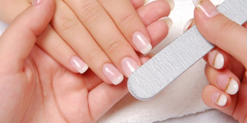 Tay người đang được dũa móng với dụng cụ chăm sóc móng trên nền vải trắng.
