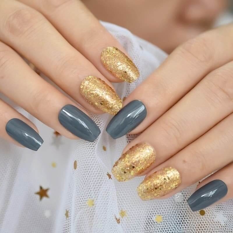 Bàn tay với móng tay sơn màu xám và kim tuyến vàng, nền vải trắng có họa tiết ngôi sao.