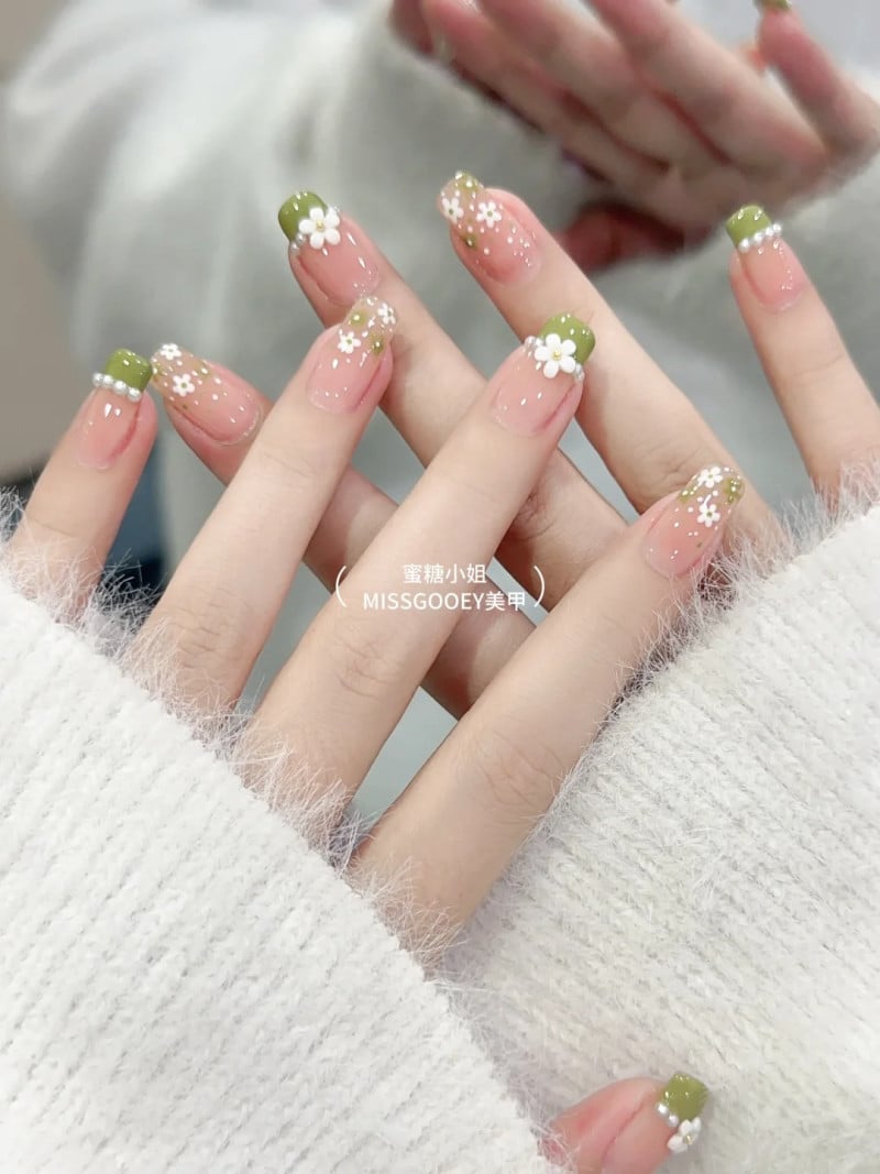 Bàn tay với móng tay sơn màu xanh và hoa văn trắng, mặc áo len màu trắng.