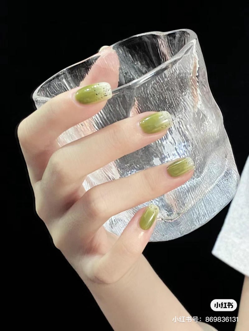 Tay cầm ly thủy tinh trong suốt, móng tay sơn màu xanh lá cây.