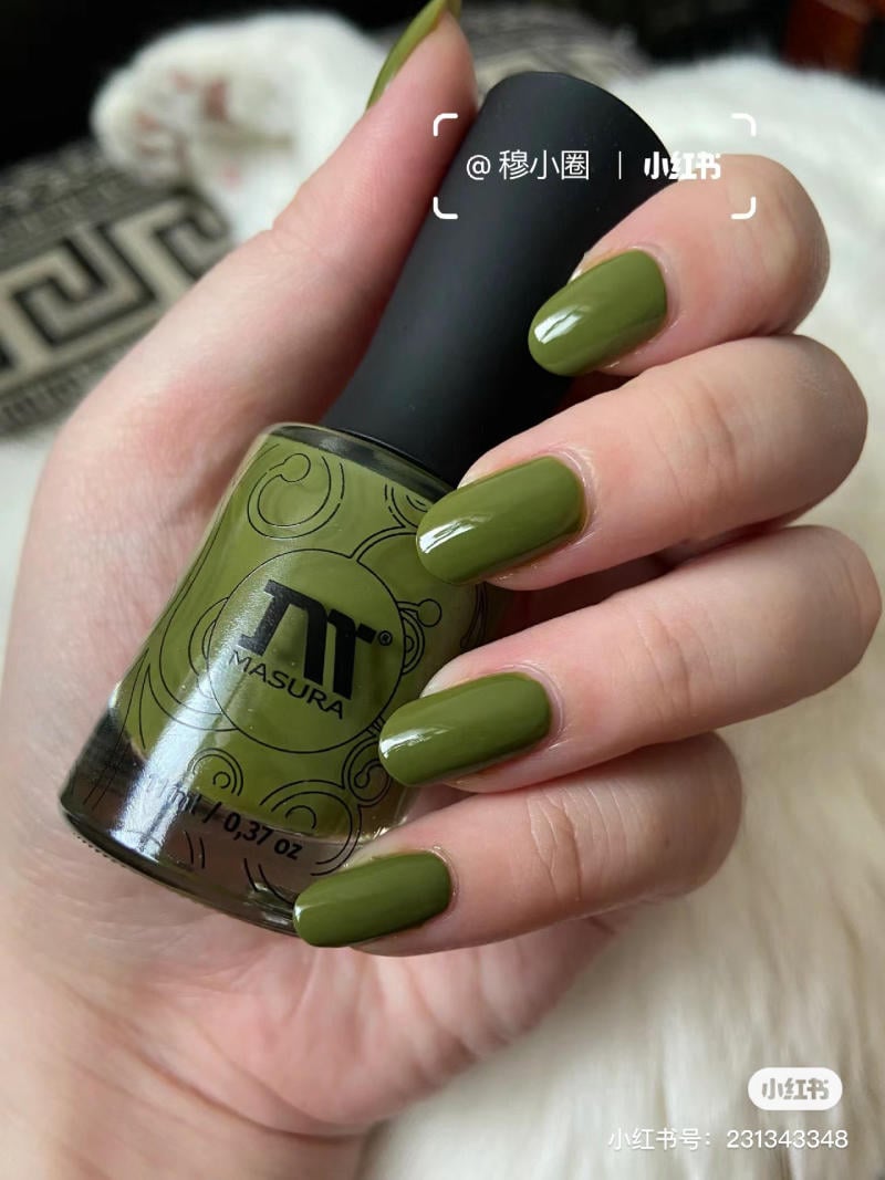 Tay cầm lọ sơn móng màu xanh lá, móng tay được sơn cùng màu, nền họa tiết vải đen trắng.