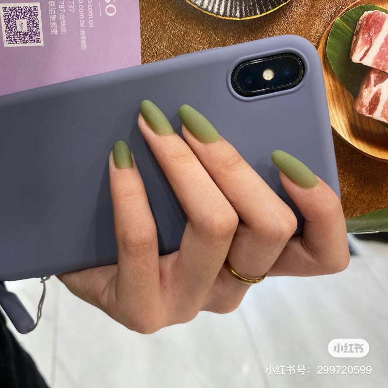 Tay cầm điện thoại có móng tay màu xanh lá mờ, bên cạnh là một tấm thiệp và đĩa thức ăn.