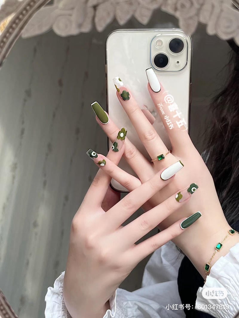 Bàn tay với móng tay được sơn màu xanh và trắng họa tiết, cầm điện thoại, phản chiếu qua gương.