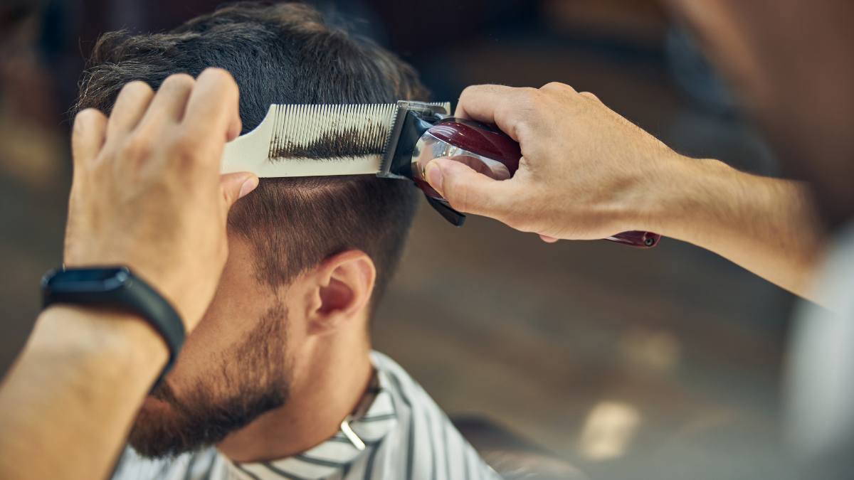 Người đang cắt tóc cho khách bằng tông đơ và lược trong tiệm cắt tóc.