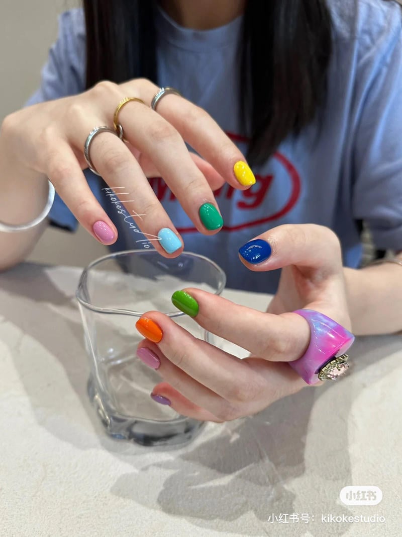 Tay cầm ly thủy tinh, m&oacute;ng tay sơn nhiều m&agrave;u sắc kh&aacute;c nhau, đeo nhẫn kim loại v&agrave; nhẫn lớn m&agrave;u hồng t&iacute;m.