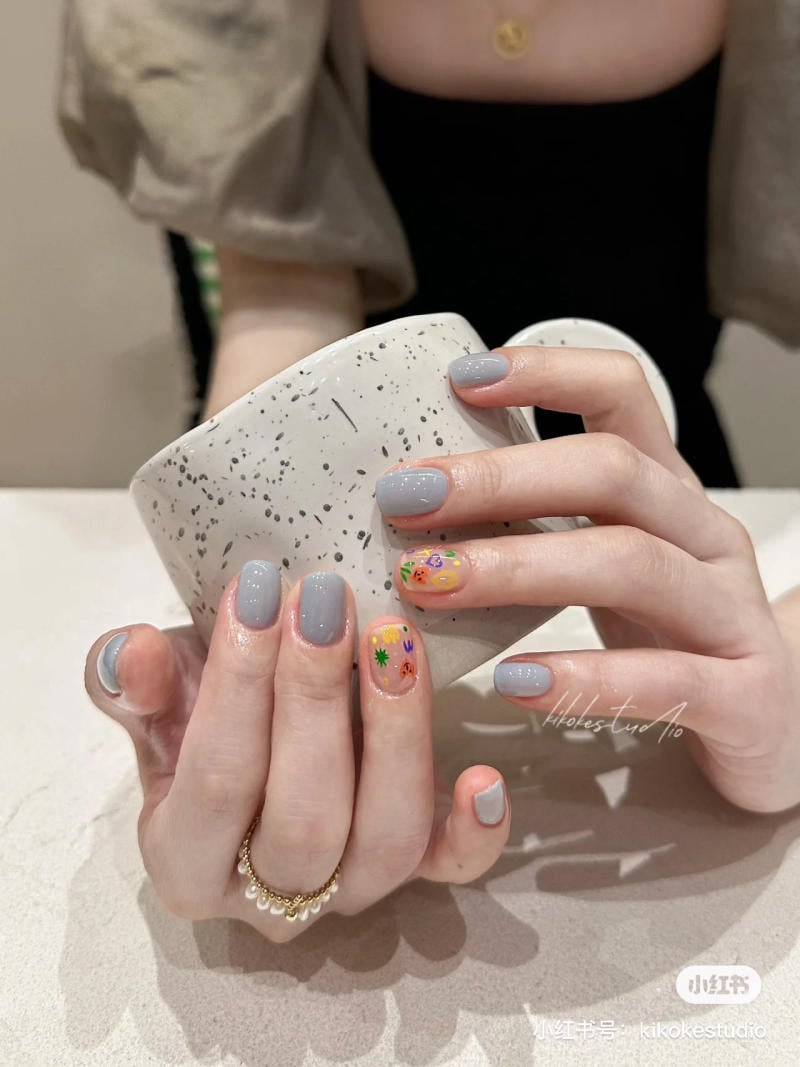 B&agrave;n tay với m&oacute;ng tay sơn m&agrave;u x&aacute;m v&agrave; họa tiết cầm cốc trắng đốm đen tr&ecirc;n nền mặt b&agrave;n s&aacute;ng m&agrave;u.