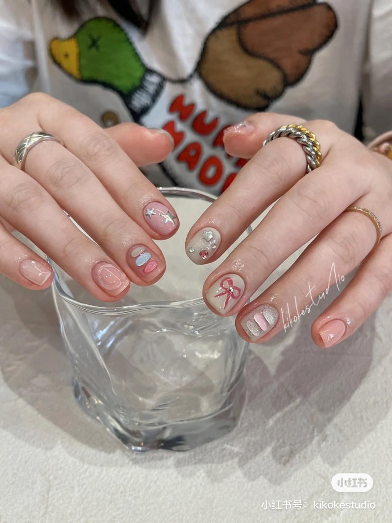 Đ&ocirc;i tay với m&oacute;ng được trang tr&iacute; họa tiết ng&ocirc;i sao v&agrave; nơ, cầm một ly thủy tinh trong suốt.