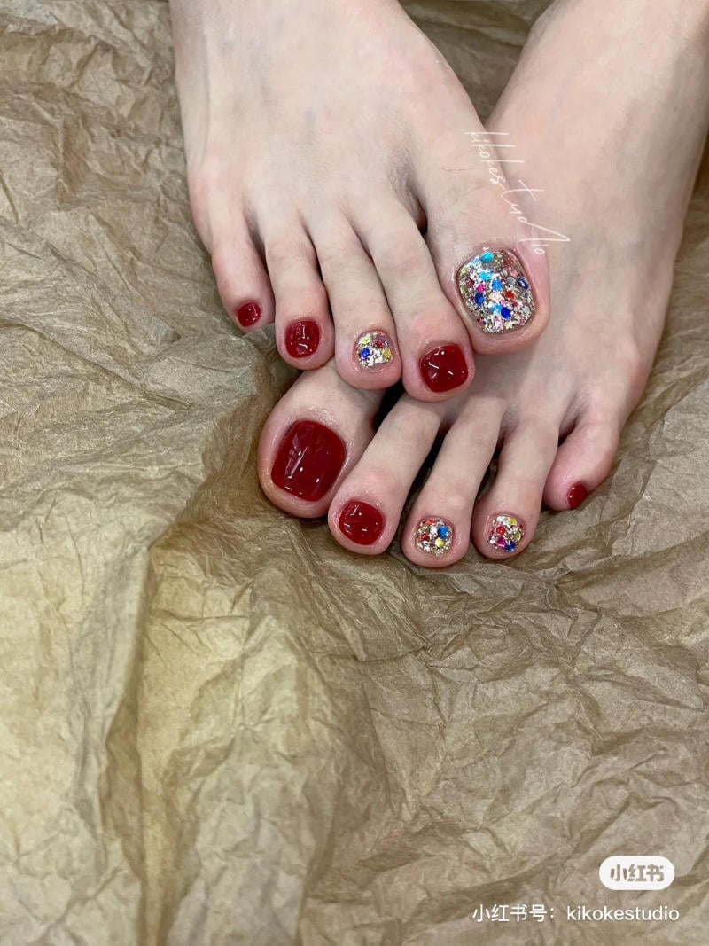 B&agrave;n ch&acirc;n với m&oacute;ng được sơn m&agrave;u đỏ v&agrave; trang tr&iacute; đ&aacute; lấp l&aacute;nh, đặt tr&ecirc;n nền giấy m&agrave;u n&acirc;u nhăn.