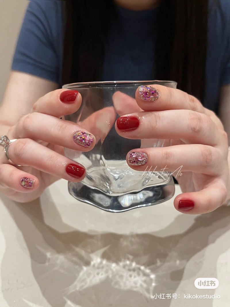 Người đang cầm ly thủy tinh với m&oacute;ng tay sơn đỏ v&agrave; &aacute;nh nhũ.