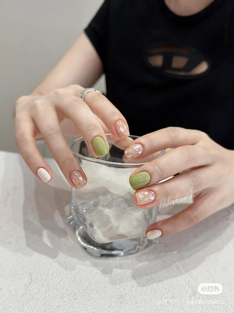 Tay với m&oacute;ng nghệ thuật đa m&agrave;u sắc cầm ly thủy tinh trong suốt tr&ecirc;n mặt b&agrave;n s&aacute;ng m&agrave;u.