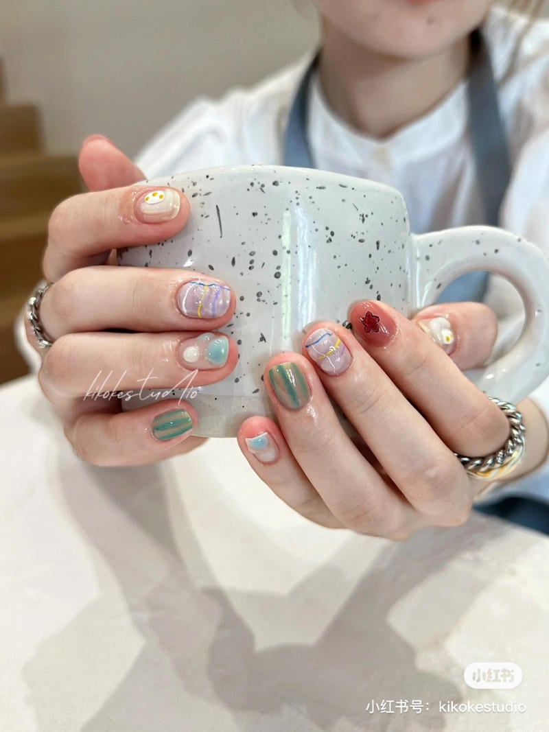 Người cầm cốc sứ trắng, m&oacute;ng tay được trang tr&iacute; nghệ thuật với nhiều m&agrave;u sắc v&agrave; họa tiết kh&aacute;c nhau.