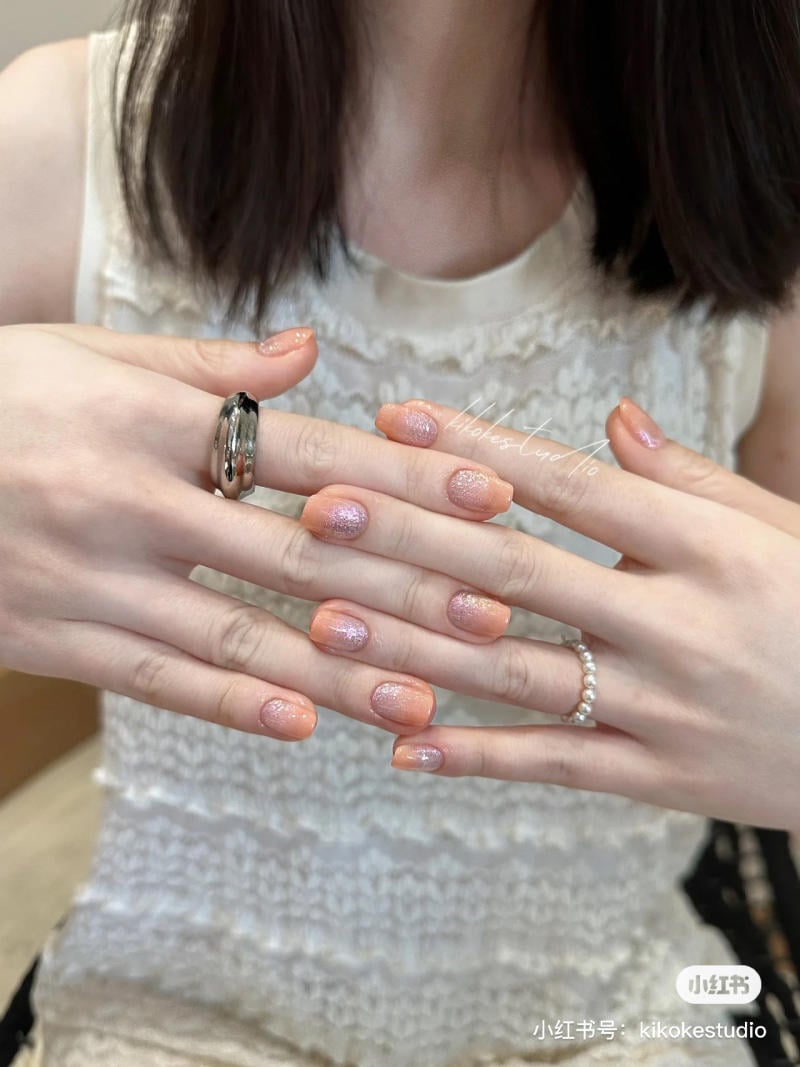 B&agrave;n tay với m&oacute;ng tay được sơn m&agrave;u cam lấp l&aacute;nh, đeo nhẫn bạc v&agrave; nhẫn ngọc trai, tr&ecirc;n nền &aacute;o ren trắng.