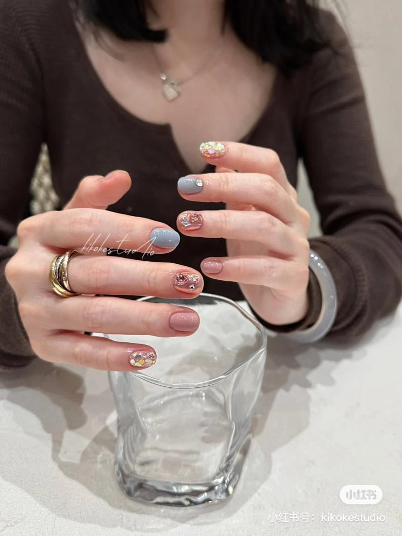 Người đeo v&ograve;ng tay, với m&oacute;ng tay được sơn trang tr&iacute;, cầm một ly thủy tinh trong suốt tr&ecirc;n b&agrave;n.