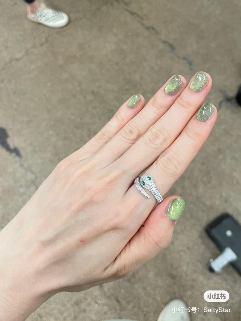 B&agrave;n tay đeo nhẫn h&igrave;nh rắn, m&oacute;ng tay sơn m&agrave;u xanh lấp l&aacute;nh, nền l&agrave; s&agrave;n b&ecirc; t&ocirc;ng v&agrave; gi&agrave;y thể thao trắng.