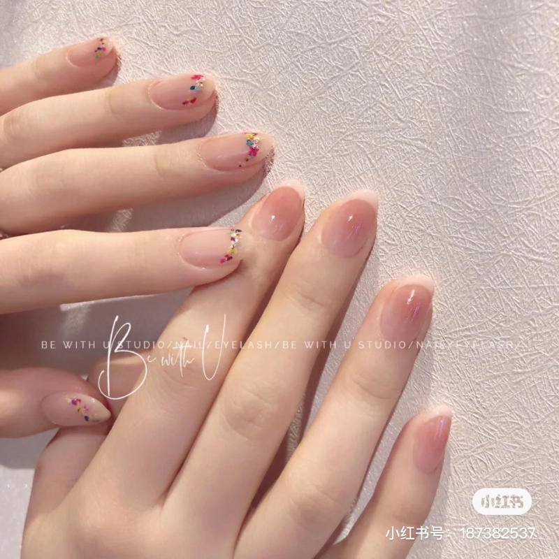 B&agrave;n tay với m&oacute;ng tay được sơn m&agrave;u nude, trang tr&iacute; họa tiết nhiều m&agrave;u ở đầu m&oacute;ng tr&ecirc;n nền vải trắng.