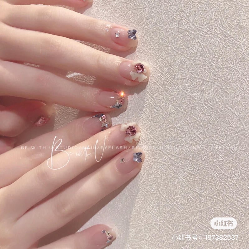 B&agrave;n tay với m&oacute;ng tay trang tr&iacute; hoa v&agrave; đ&aacute; qu&yacute; tr&ecirc;n nền trắng c&oacute; họa tiết.