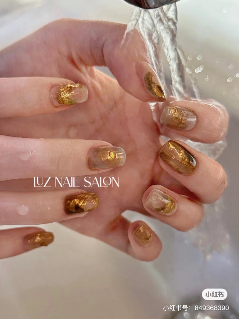 B&agrave;n tay với m&oacute;ng nghệ thuật &aacute;nh v&agrave;ng dưới d&ograve;ng nước chảy nhẹ, tạo cảm gi&aacute;c sang trọng v&agrave; tinh tế.